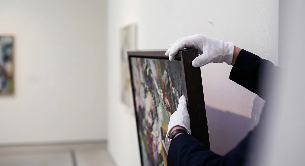 Manutentionnaire ganté décrochant délicatement un tableau d’un mur